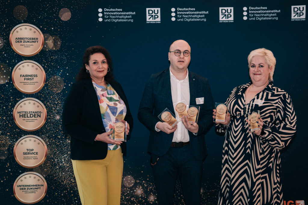 Drei Personen stehen mit Auszeichnungen vor einem dunkelblauen Hintergrund. An der Seite sind die fünf Auszeichnungen in groß, oben steht "Deutsches Innovationsinstitut für Nachhaltigkeit und Digitalisierung"