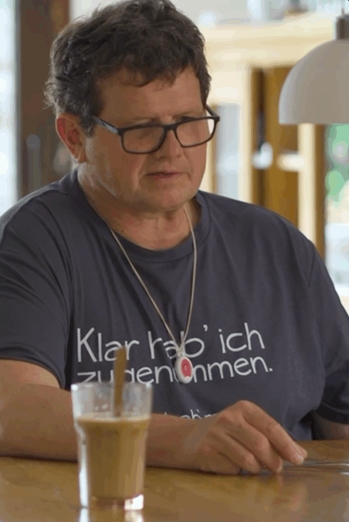 Portraitaufnahme von einem Mann mit grauem Shirt, Brille und kurzen dunklen Haaren schaut nach unten.