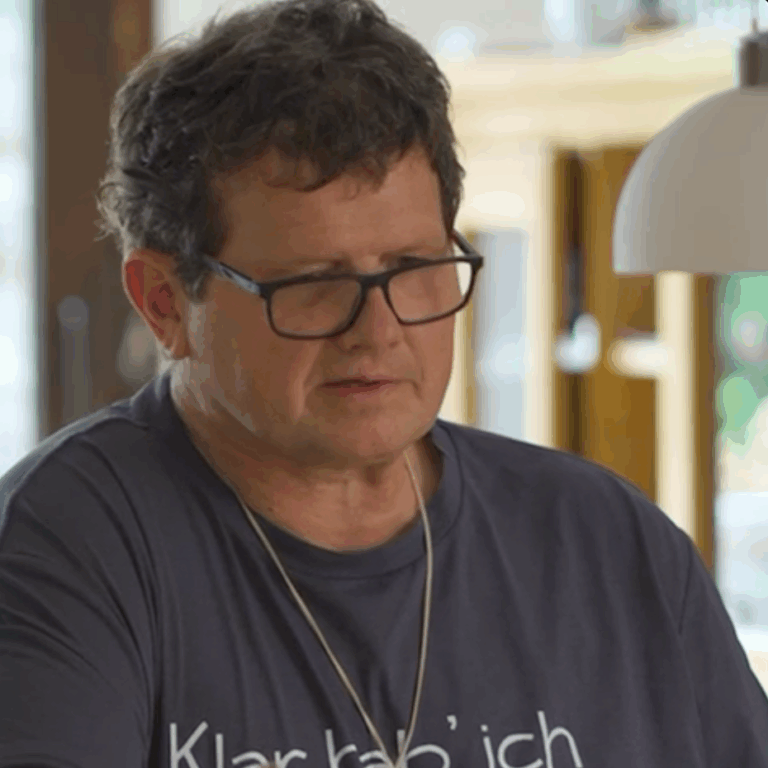 Portraitaufnahme von einem Mann mit grauem Shirt, Brille und kurzen dunklen Haaren schaut nach unten.