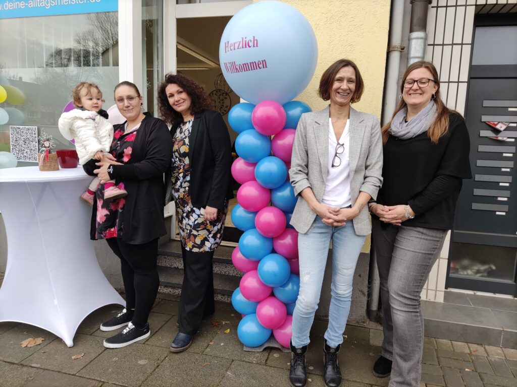 Zwei Frauen stehen rechts von einem Luftballon Aufsteller und lachen. Auf der linken Seite stehen zwei weitere Frauen, während eine ein Baby auf dem Arm hält.