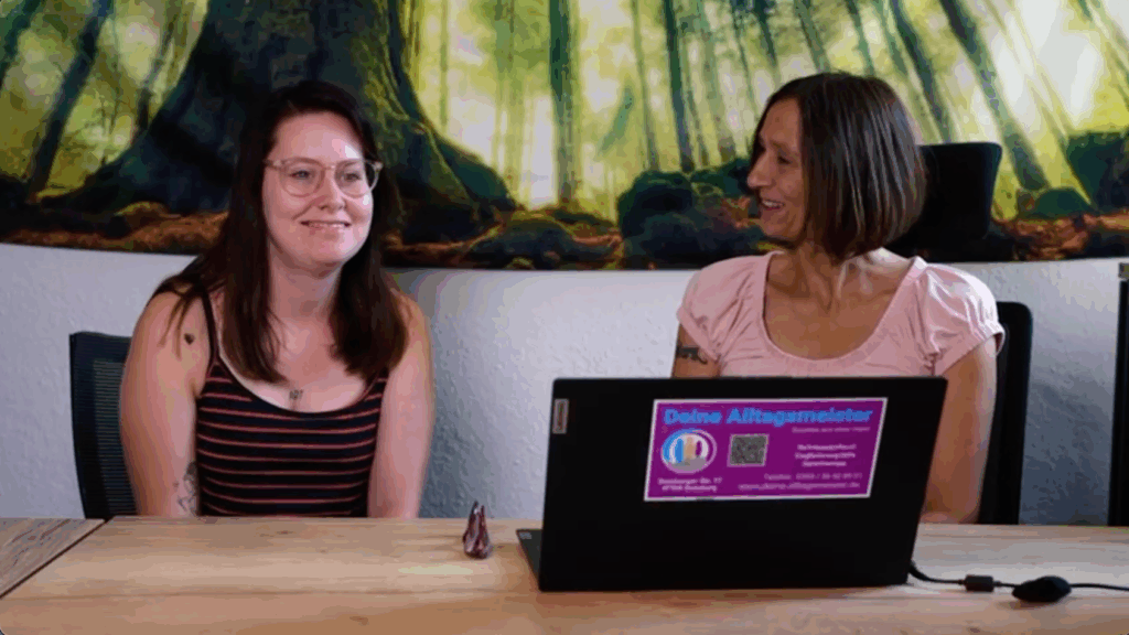 Junge Frau in gestreiftem Top, langen dunklen Haaren und Brille lächelt am Tisch