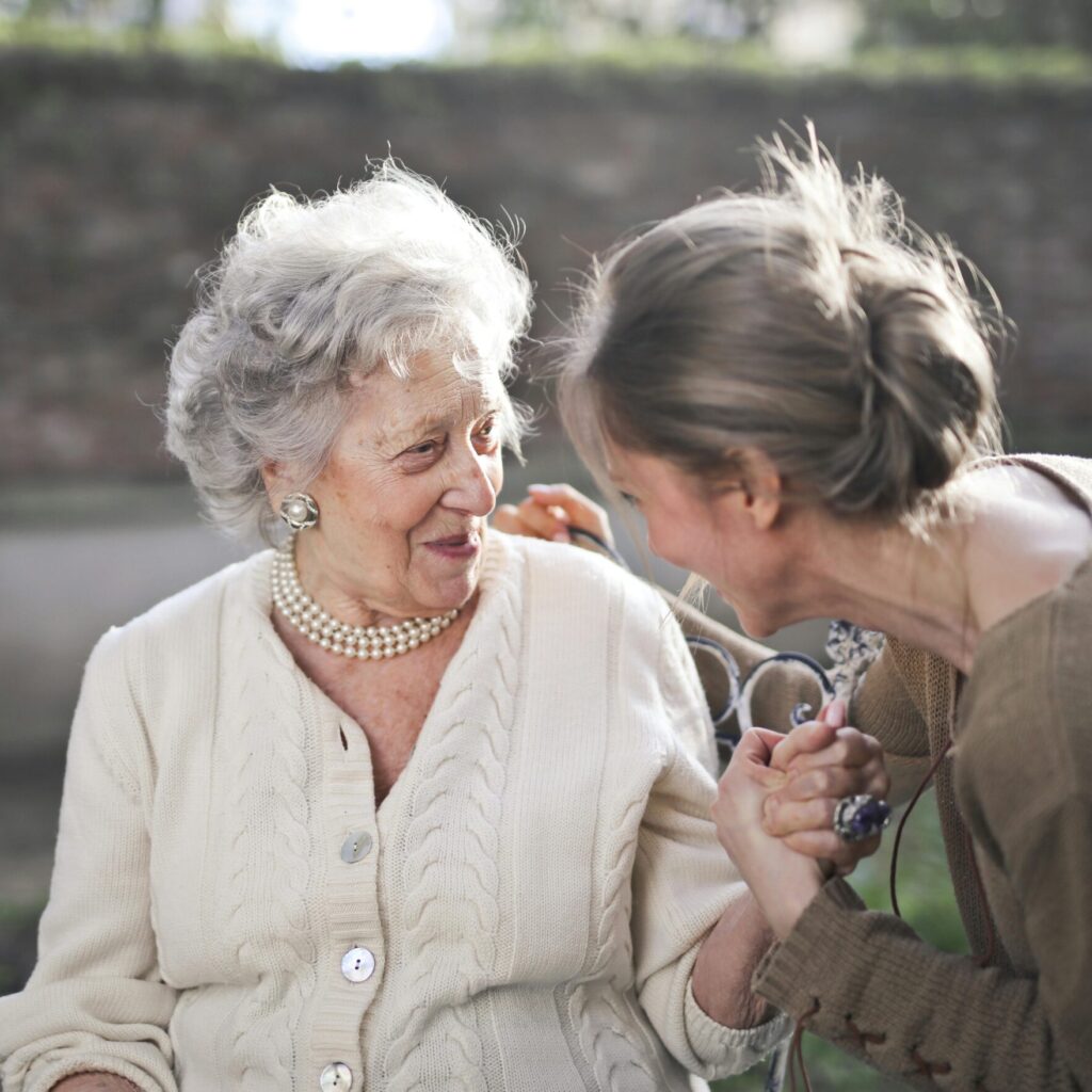 Eine junge und ältere Frau schauen sich an, halten die Hände und lächeln.