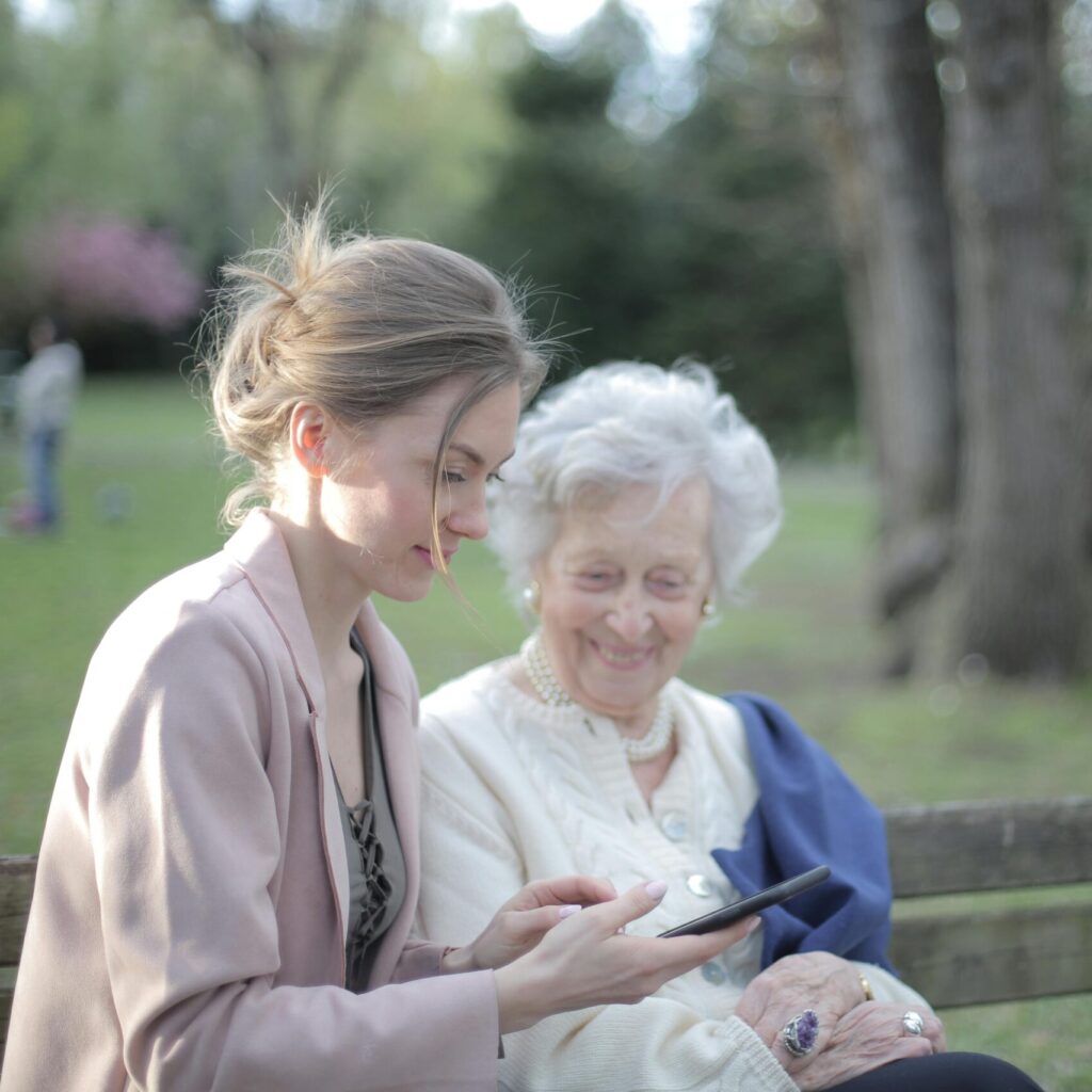 Junge Frau zeigt einer älteren Frau etwas auf dem Smartphone im Park.