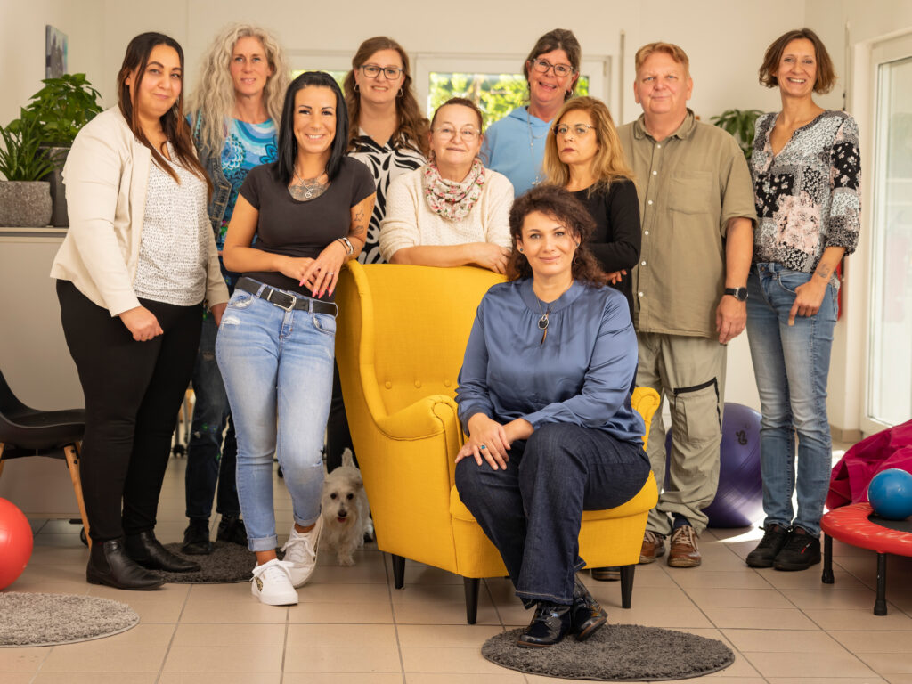 10 Personen stehen um bzw. sitzen auf einem gelben Sessel für ein Gruppenbild
