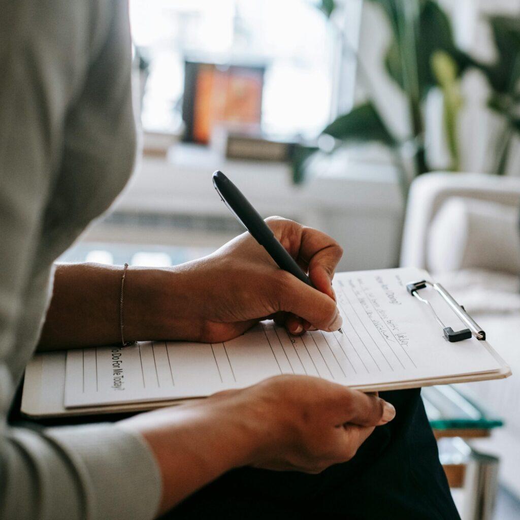 Person schreibt etwas auf ein Papier im Klemmbrett.
