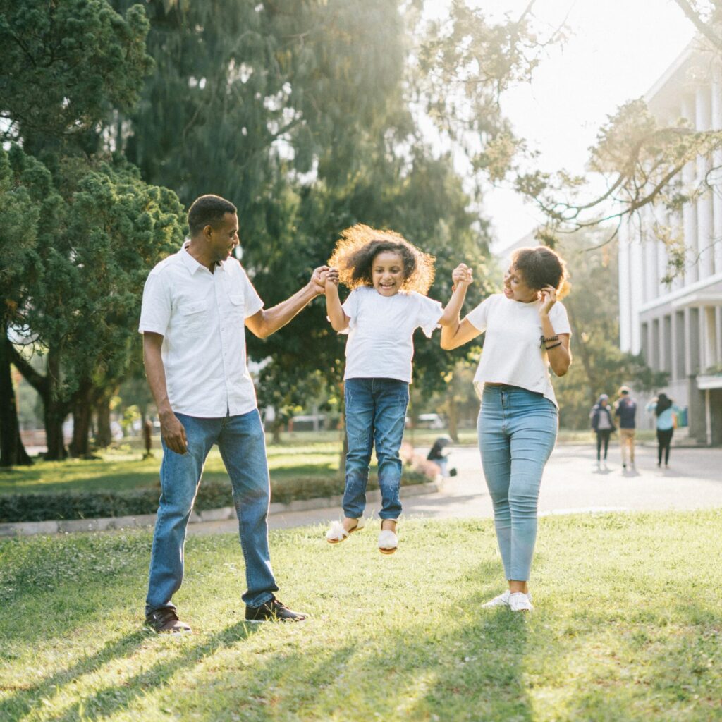 zwei Erwachsene im Park heben ein Kind hoch