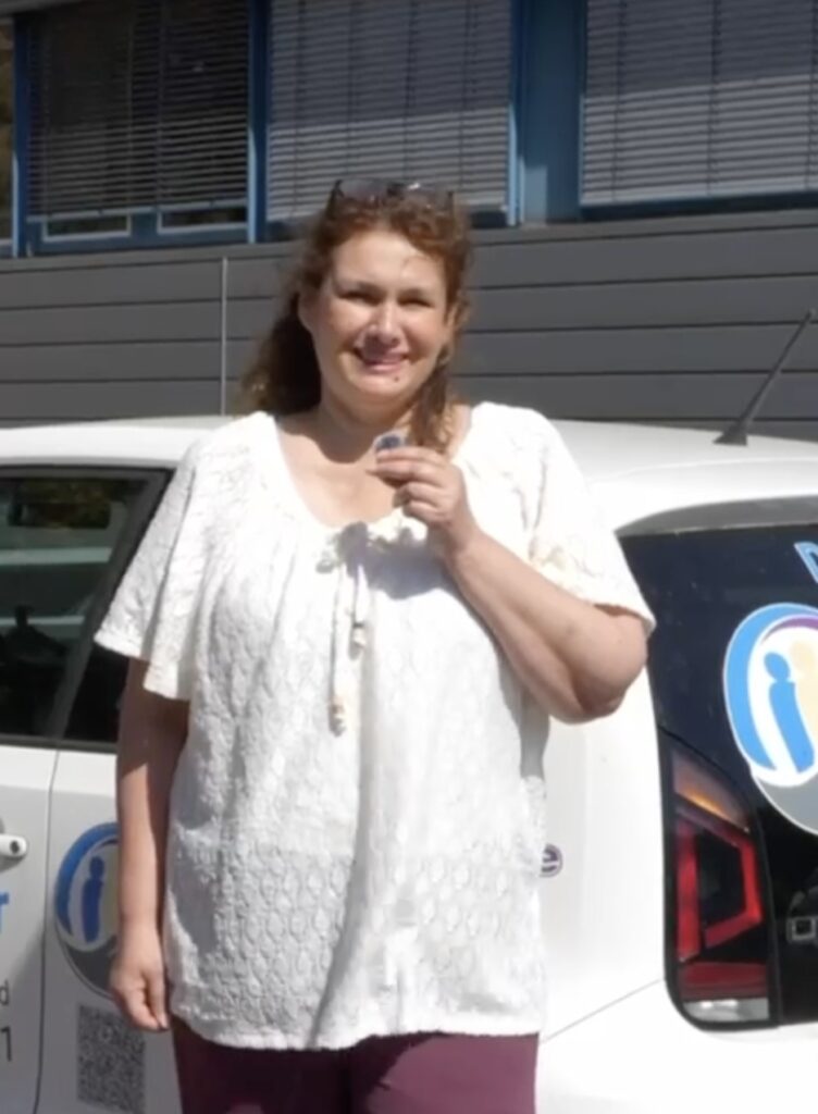 Frau Wagner Matthes steht vor einem weißen Auto mit "Deine Alltagsmeister" Logo