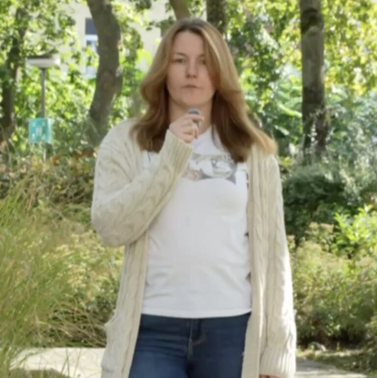 Frau mit langen Haaren steht im Wald und hält ein Mikro.